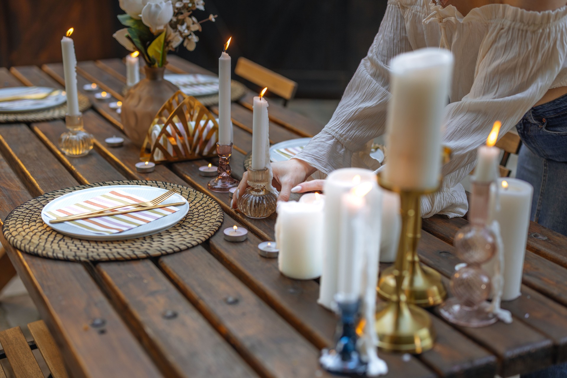 Woman arranging candles on a table set for four outdoors