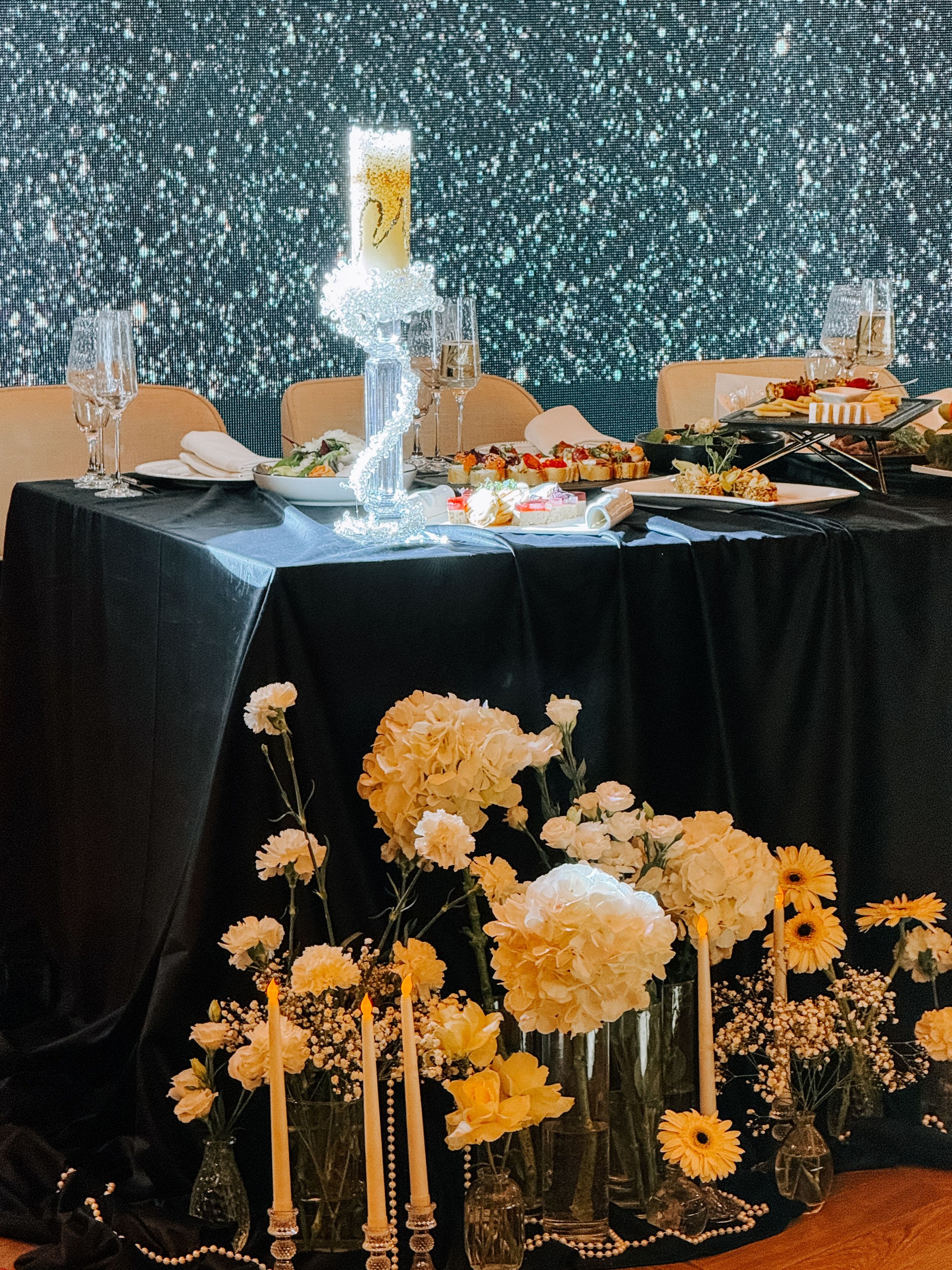 Elegant banquet table setting with decorative flowers and shimmering backdrop at evening event
